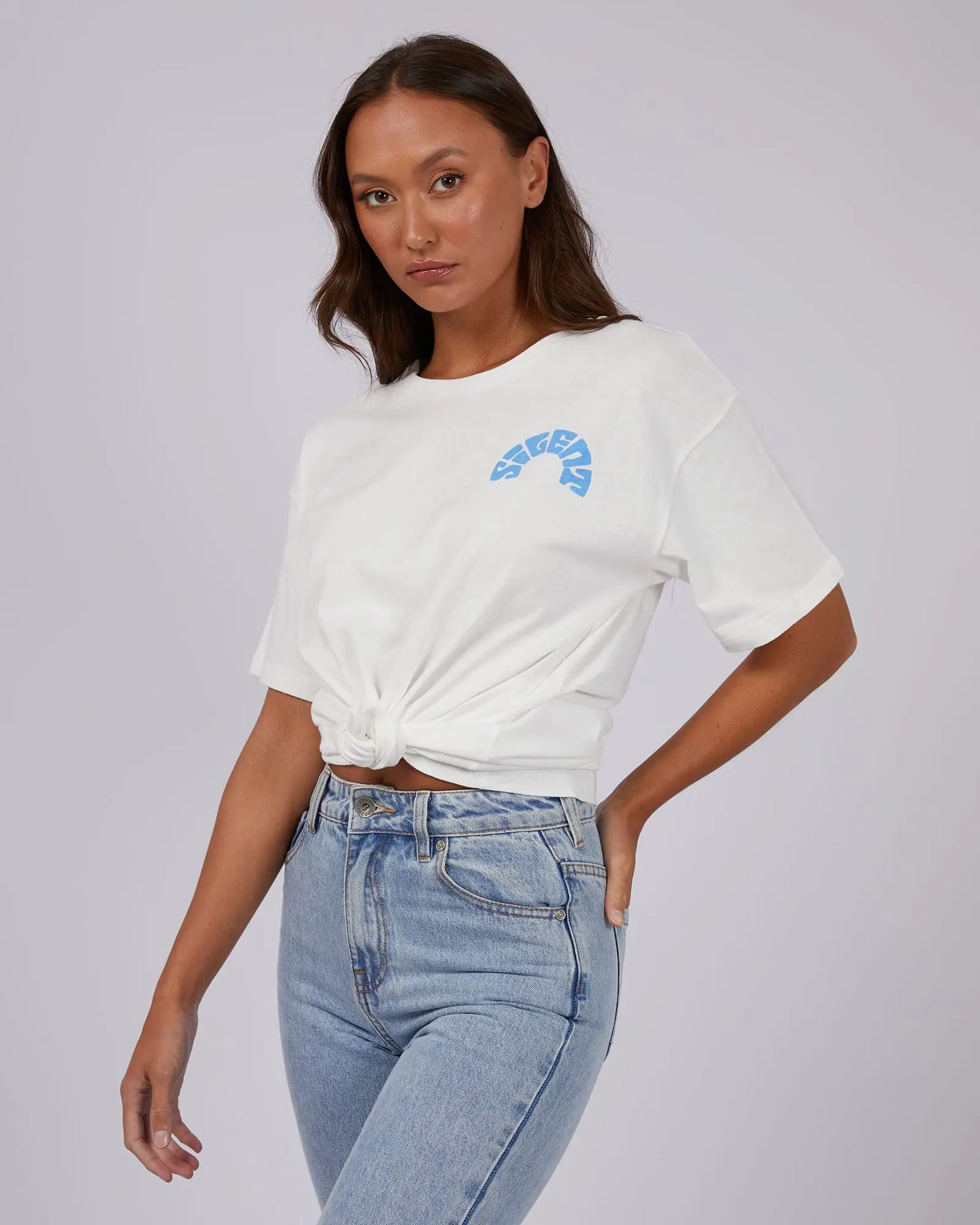 Woman wearing a white t-shirt with a blue graphic and high-waisted jeans on a plain background