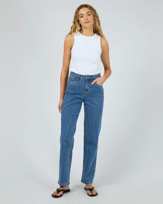 Woman wearing a white tank top and blue jeans on a plain background