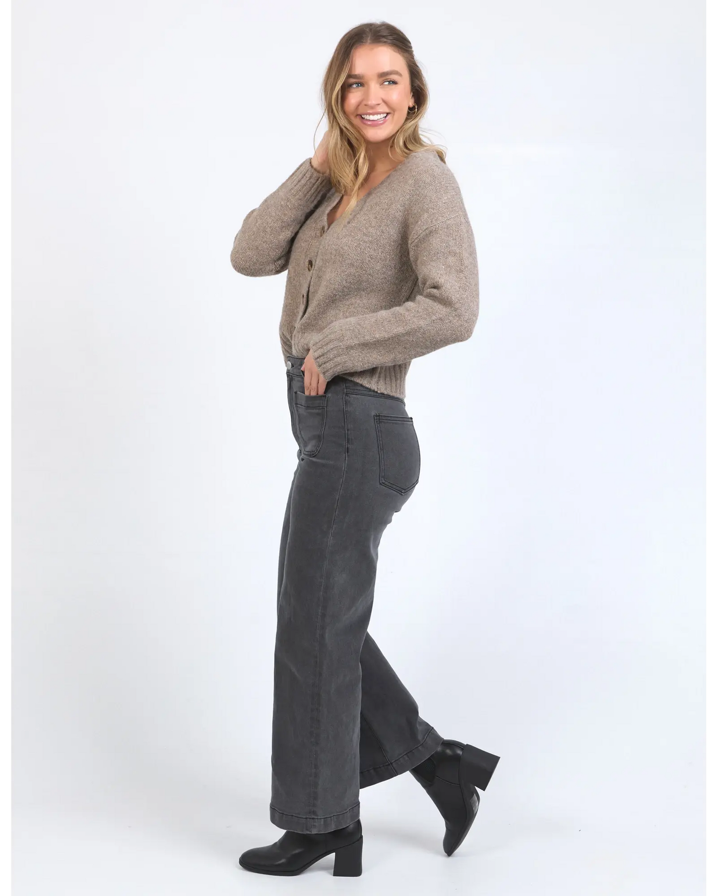 Woman wearing a brown cardigan and gray pants on a white background