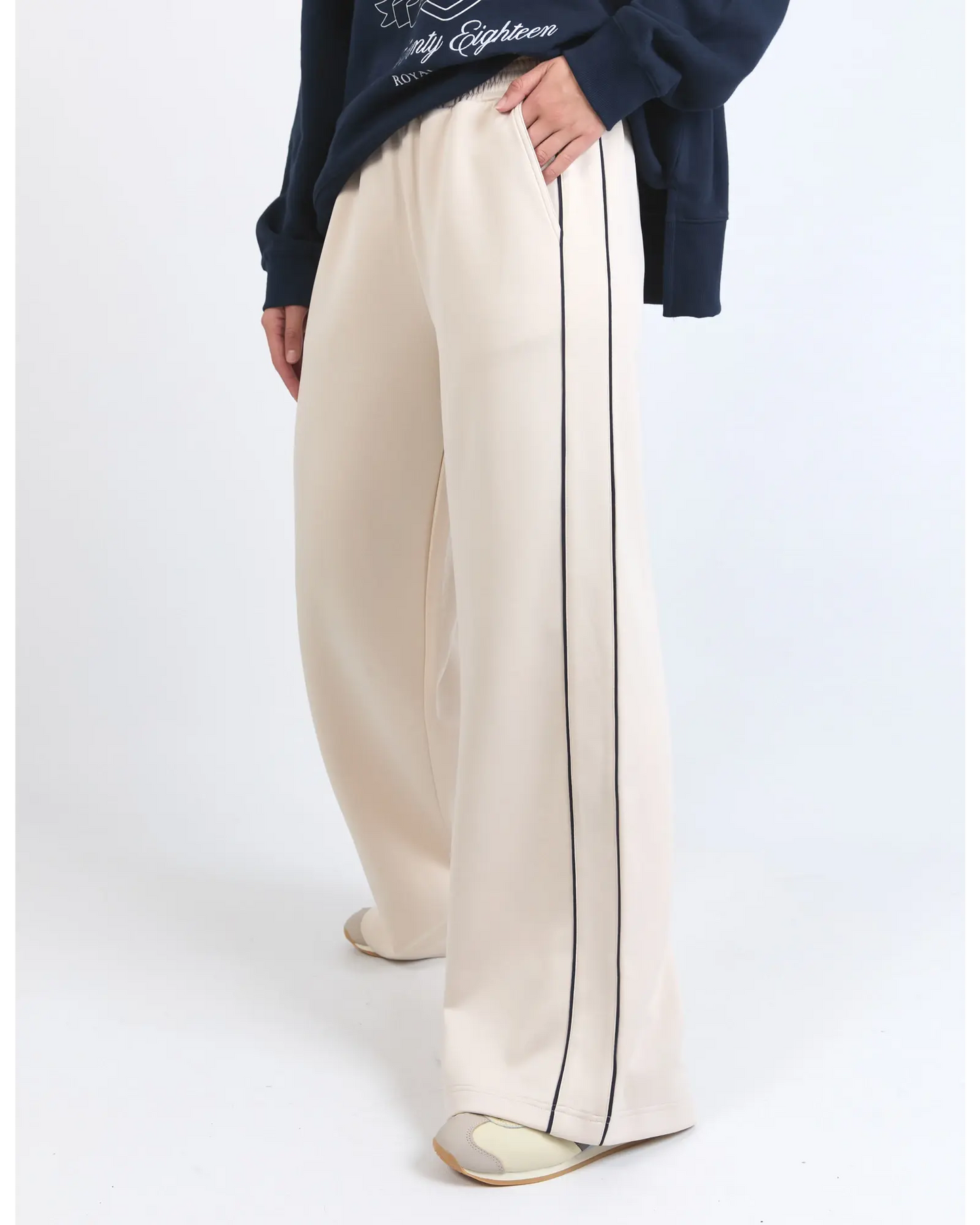 Beige wide-leg pants with a black stripe worn by a person on a white background