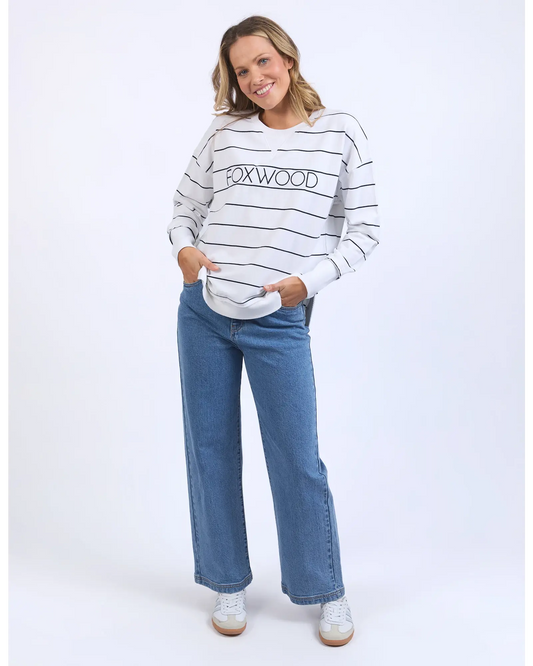 Woman wearing a striped sweater with 'Foxwood' branding and blue jeans on a white background