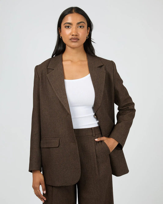 Woman wearing a brown suit with a white top on a plain background