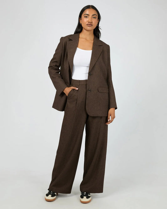 Woman wearing a brown suit with a white top on a plain background