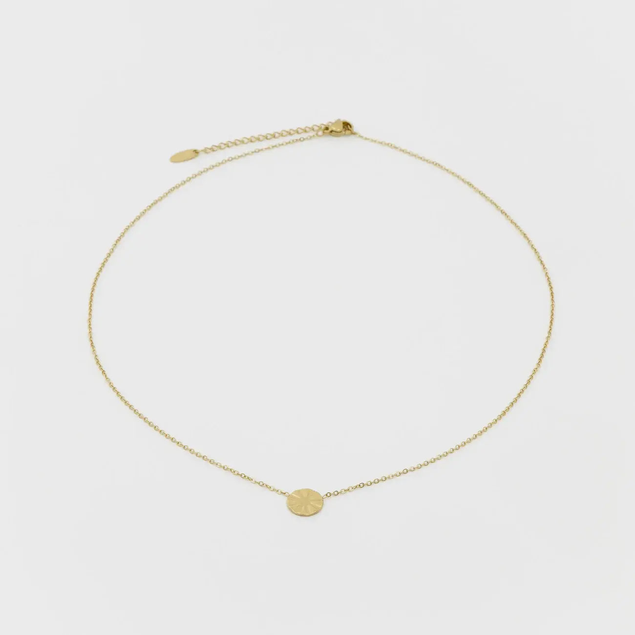 Gold necklace with a small round pendant on a light gray background