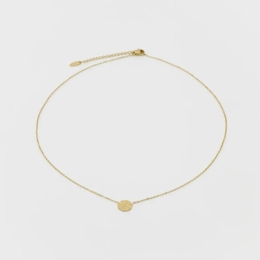 Gold necklace with a small round pendant on a light gray background