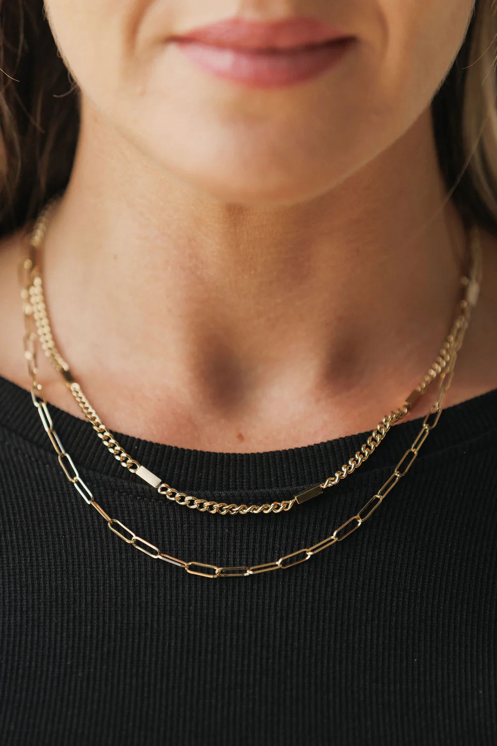 Close-up of a person wearing two gold chain necklaces on a black background - Clementine Necklace Gold - The Rose Edit
