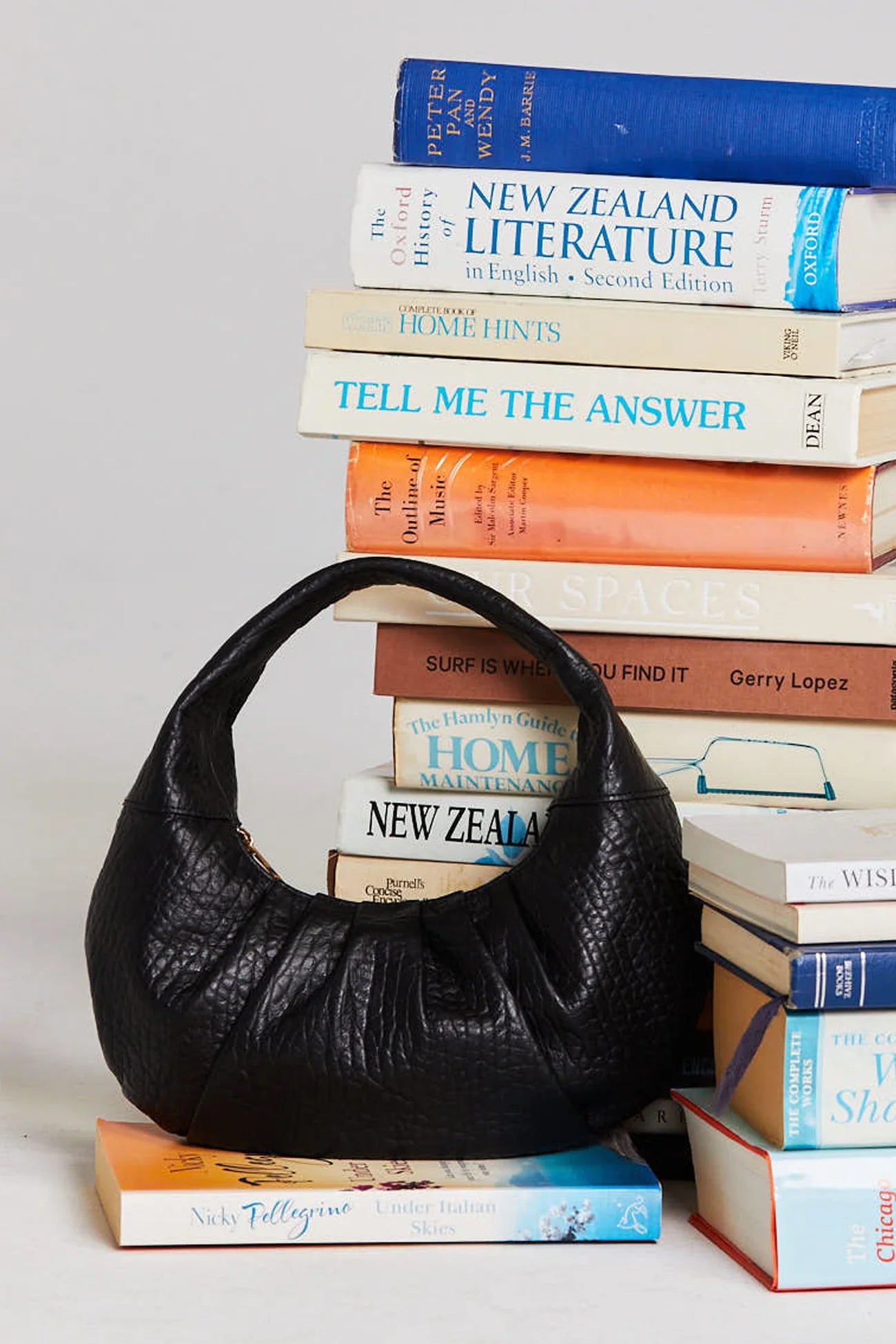 Black leather handbag on a stack of books with visible titles.