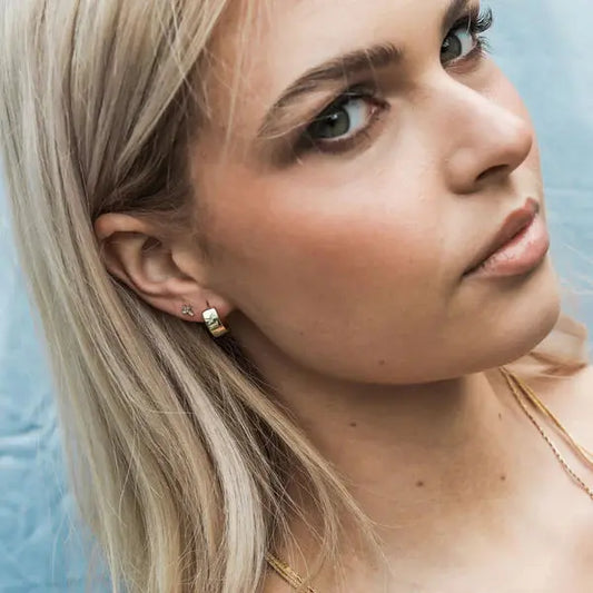 Close-up of a woman wearing gold earrings and a necklace against a light blue background