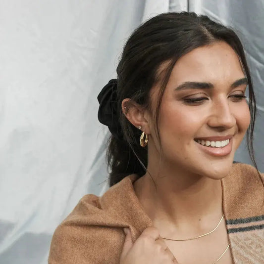 Woman with a smile wearing a brown coat against a neutral background