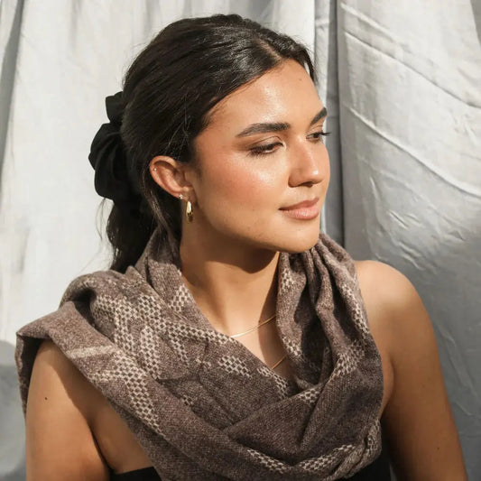 Woman wearing a brown patterned scarf against a white curtain background