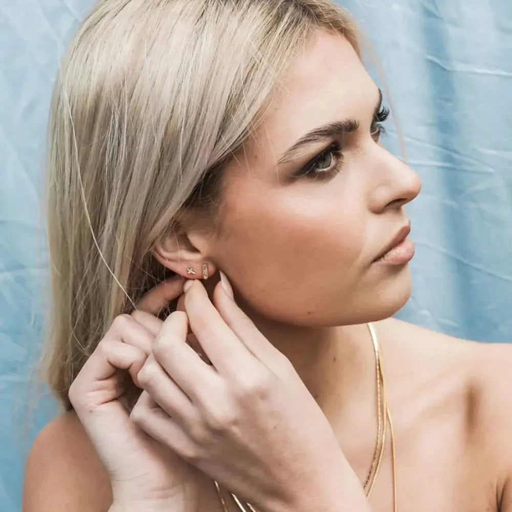 Woman adjusting an earring against a light blue background
