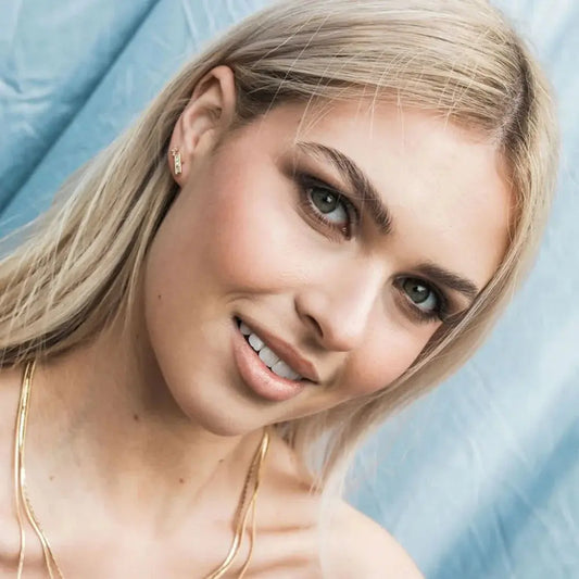 Close-up of a woman with blonde hair and blue eyes against a light blue background