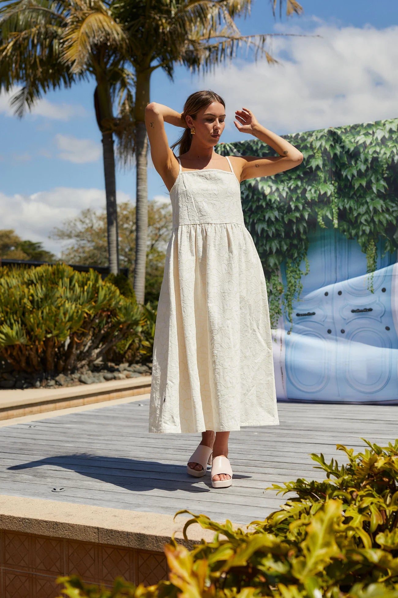 Woman in a white dress standing outdoors with palm trees and a car in the background