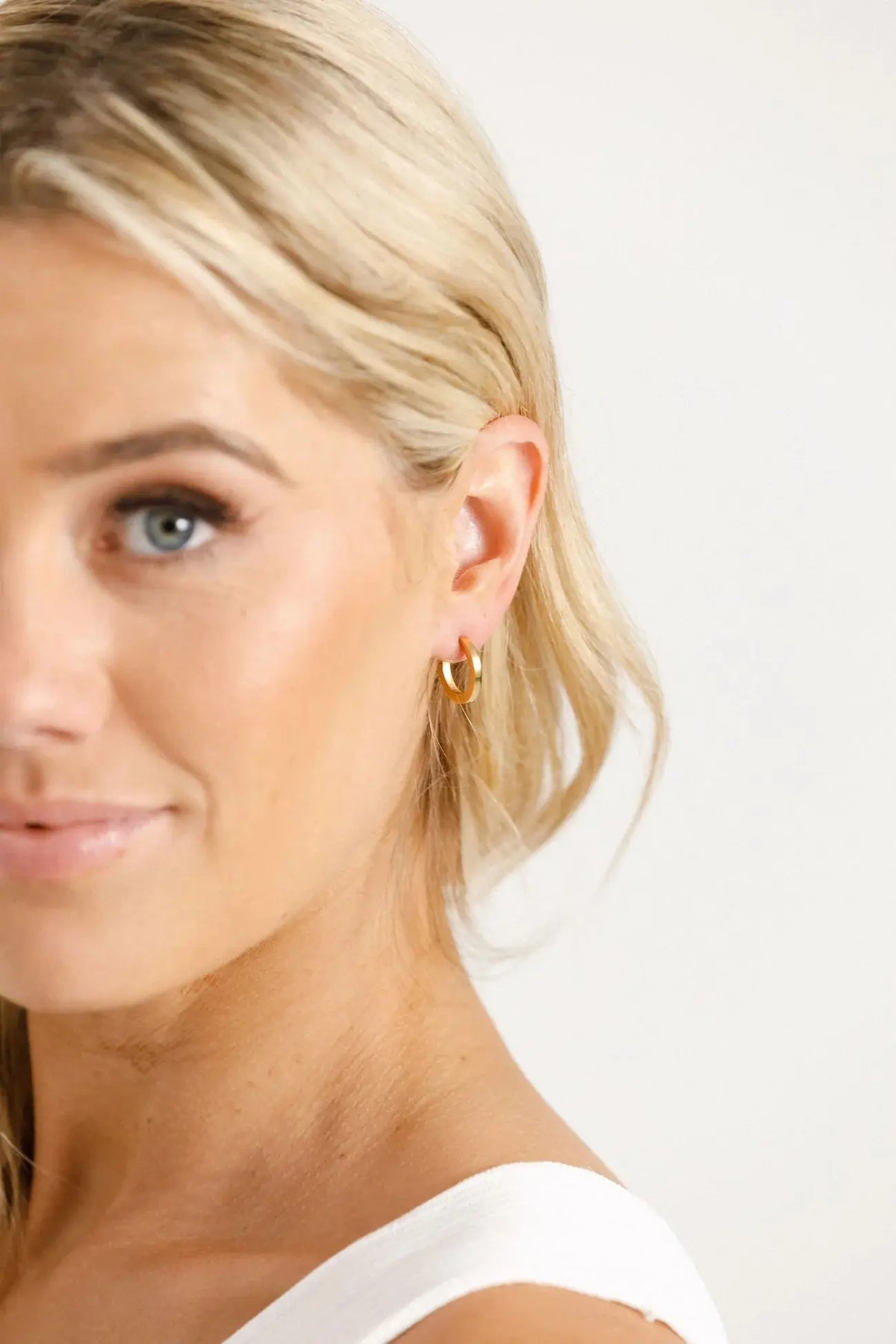 Close-up of a woman wearing gold hoop earrings with a plain background