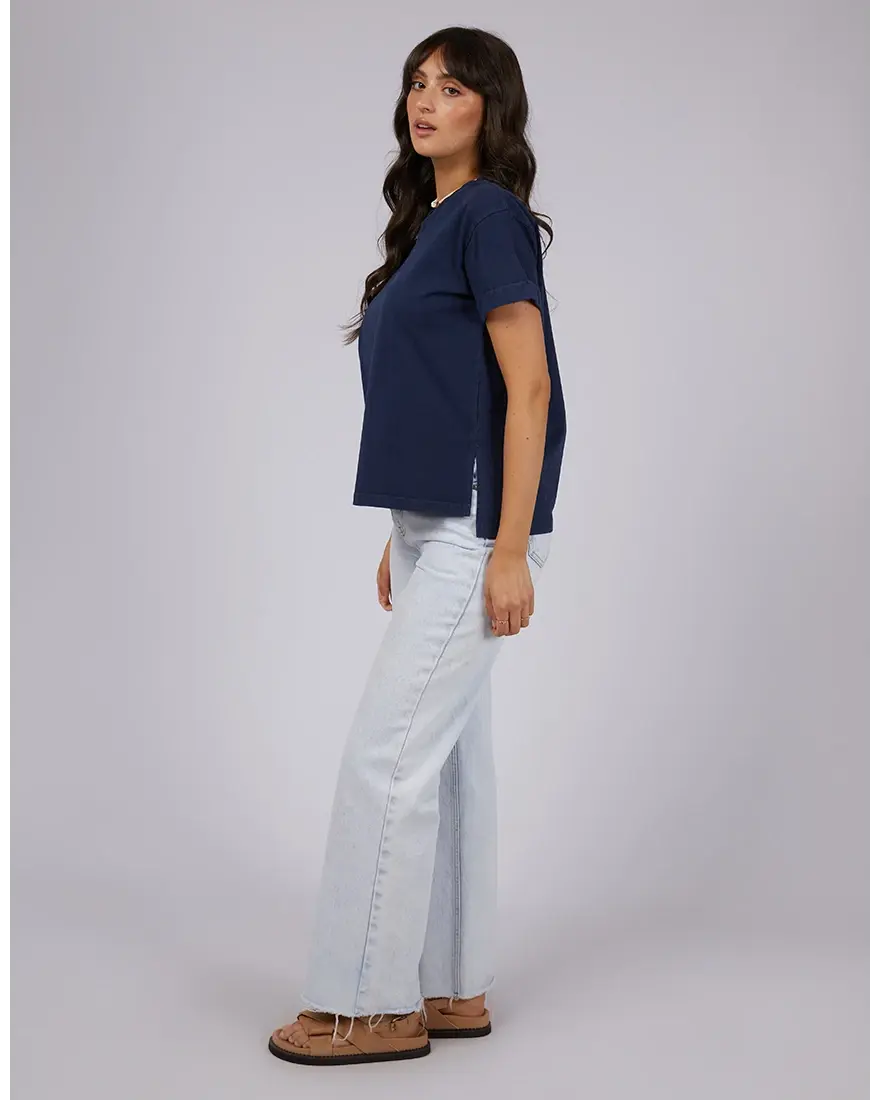 Woman wearing a navy blue t-shirt and light blue jeans on a gray background