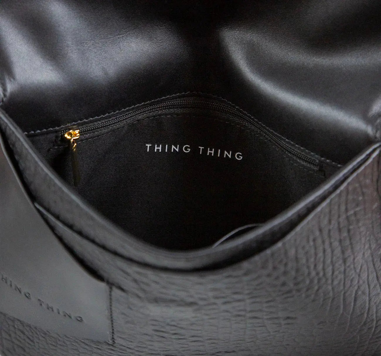 Close-up of a black leather bag with 'THING' branding.