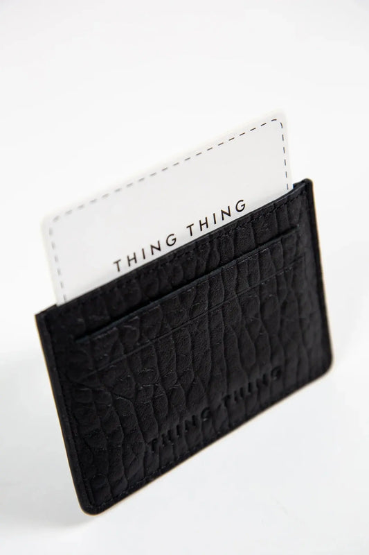 Black textured cardholder with a white card featuring 'THING THING' branding on a light gray background.