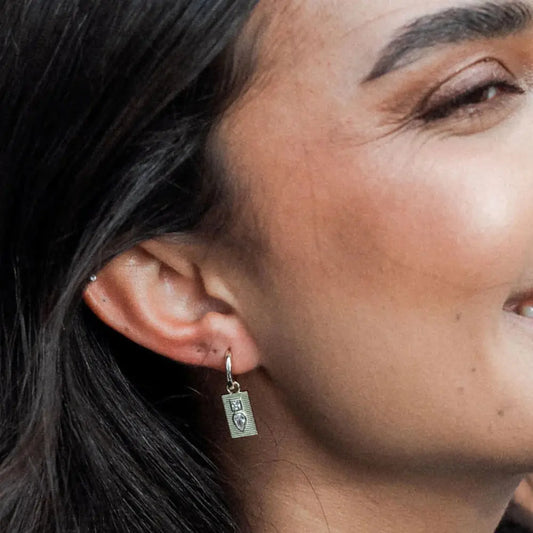 Close-up of a person wearing a silver earring with a small pendant.