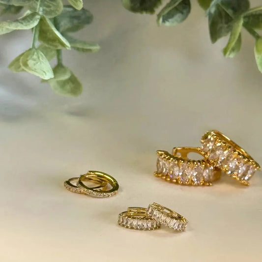 Gold rings with diamond accents on a light surface with green leaves in the background