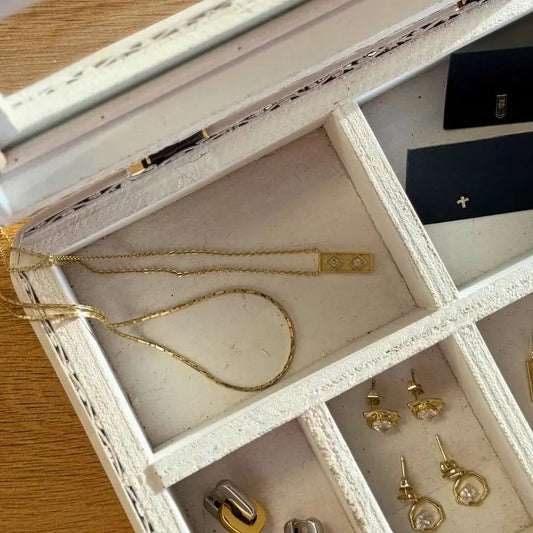 Open jewelry box with gold necklaces and earrings on a wooden surface