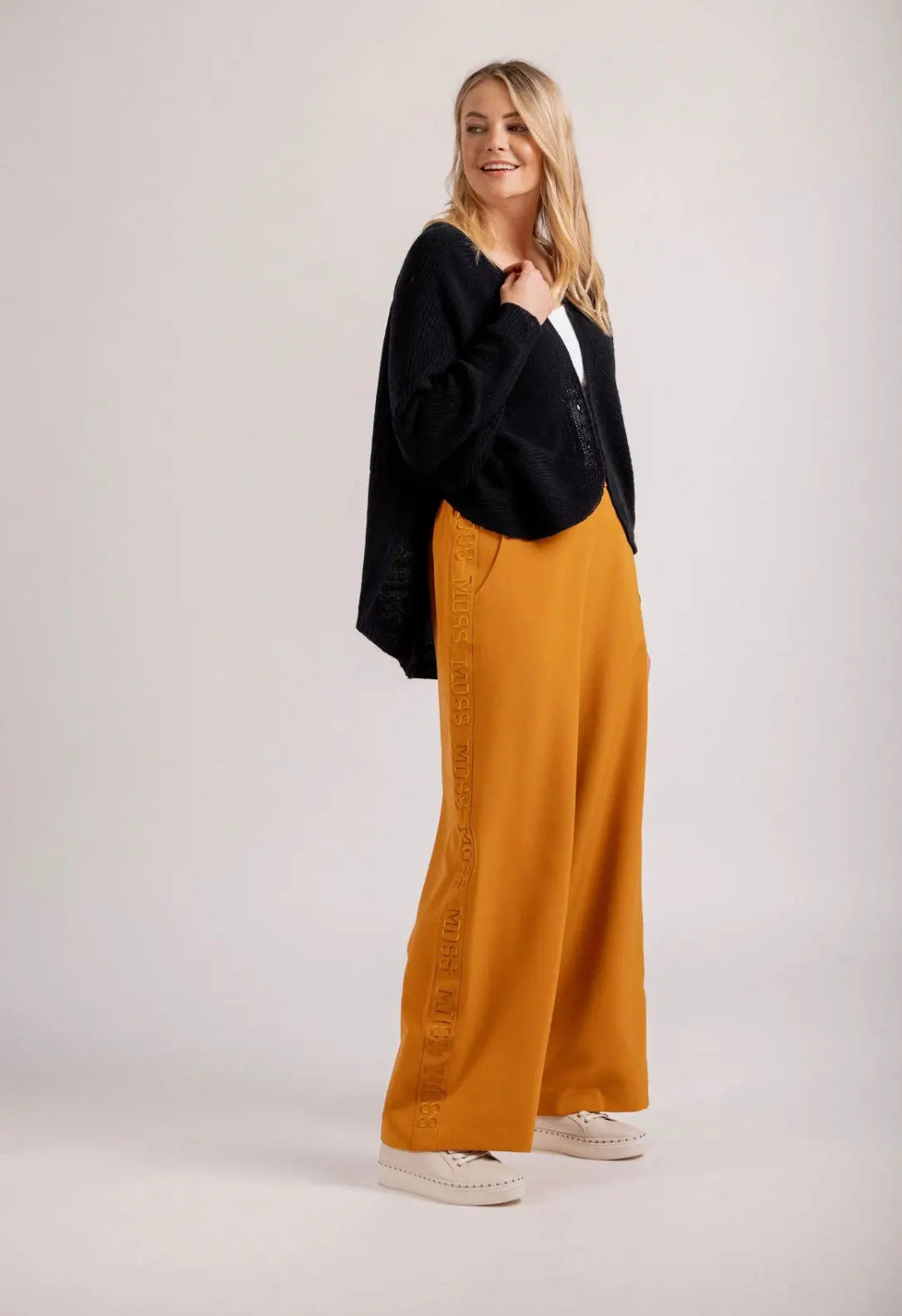 Woman wearing a black sweater and mustard yellow pants on a white background