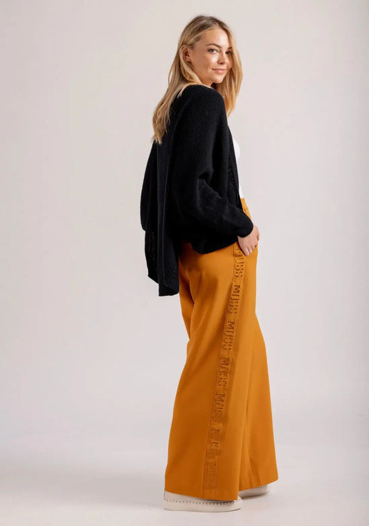 Woman wearing a black top and mustard yellow pants on a white background