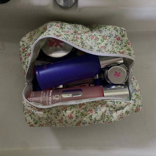 Floral-patterned makeup bag with cosmetic items on a white surface. Buttermilk Grace Carry All Bag Secret Garden - The Rose Edit