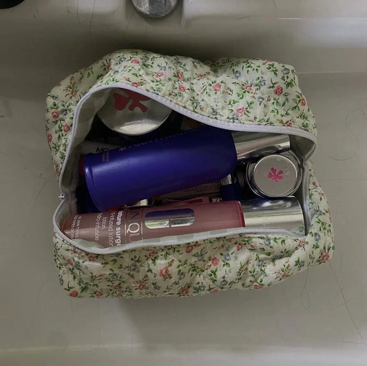 Floral-patterned makeup bag with cosmetic items on a white surface. Buttermilk Grace Carry All Bag Secret Garden - The Rose Edit