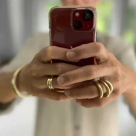 Person holding a red phone with gold rings and bracelet on fingers