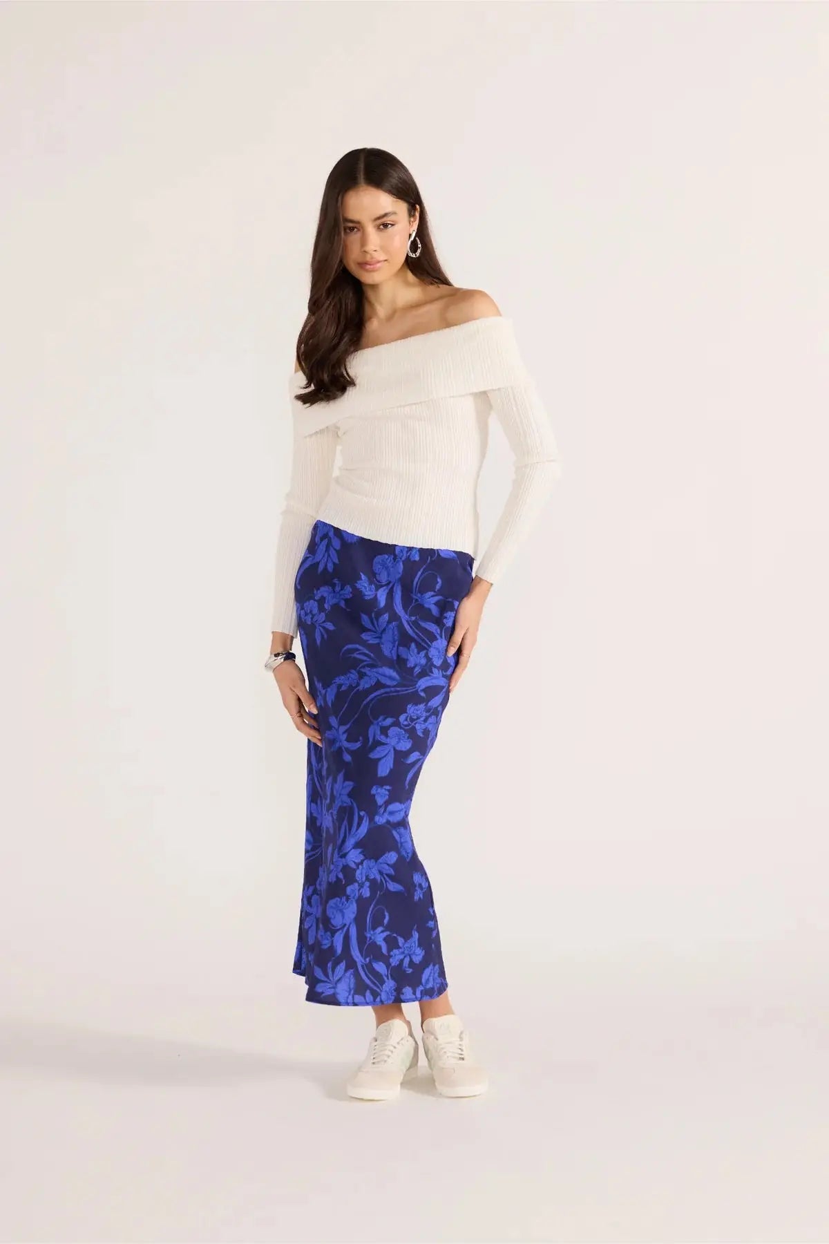 Woman wearing a white off-shoulder top and blue floral skirt on a white background