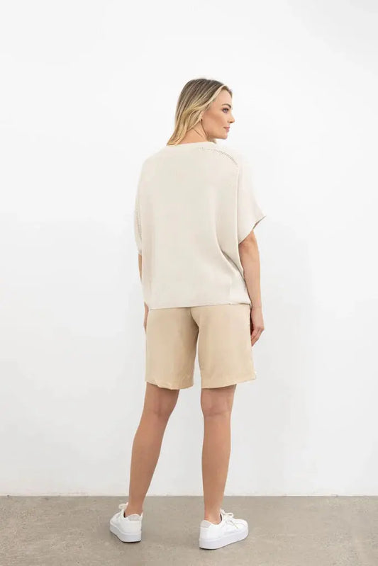 Woman wearing a beige outfit with shorts and a top against a white background