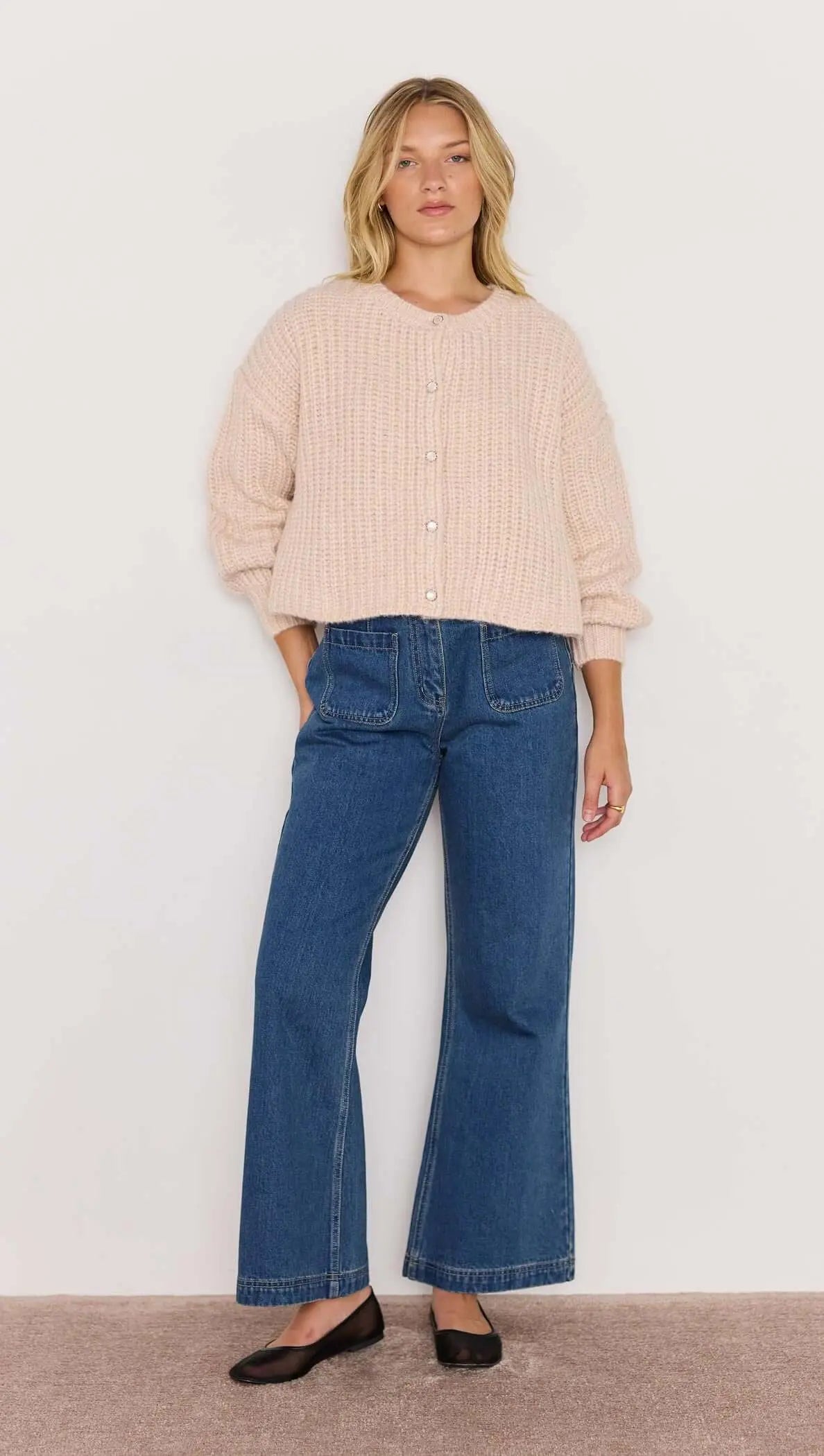 Woman wearing a beige sweater and blue jeans against a white background