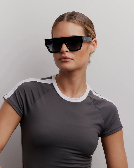 Woman wearing a gray t-shirt with white trim and black sunglasses against a plain background