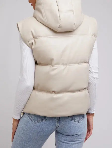 Person wearing a beige puffer vest over a white shirt and blue jeans on a light gray background