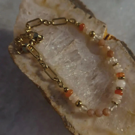 Gold bracelet with orange beads on a textured surface