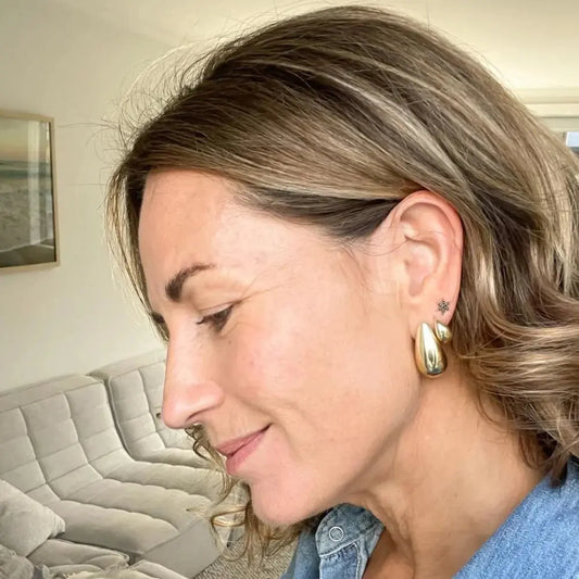 Close-up of a woman wearing gold hoop earrings with a neutral background