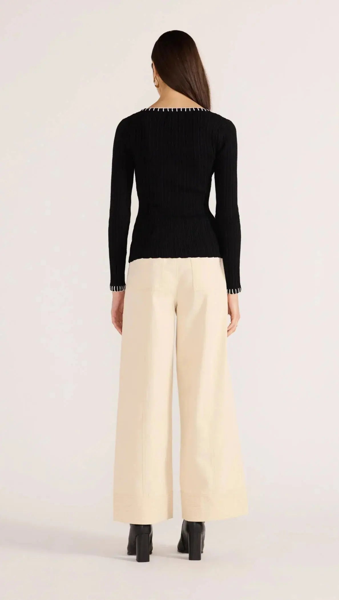 Woman wearing a black long-sleeve top and beige wide-leg pants on a white background