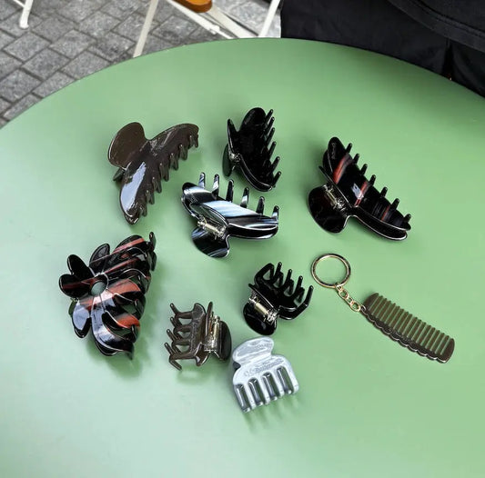 Collection of hair accessories including clips and a keychain comb on a green surface. Buttermilk Elle Claw Clip Dark Roast - The Rose Edit