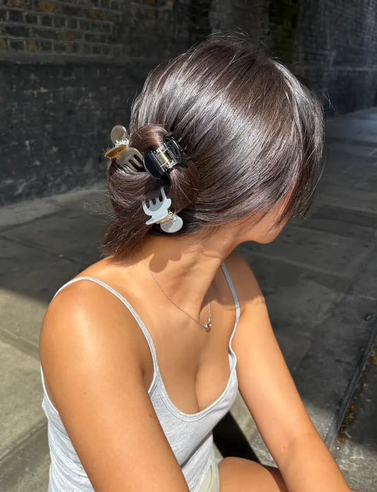 Person with styled hair sitting outdoors on a stone pavement. Buttermilk Sam Claw Clip Dark Roast - The Rose Edit