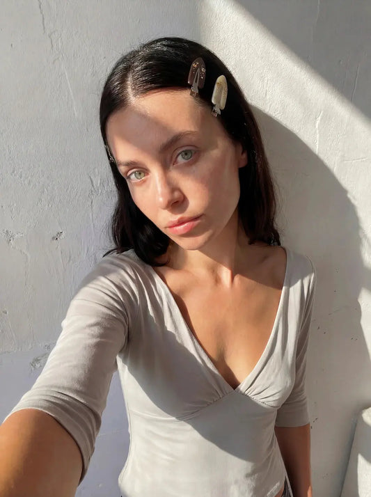 Woman wearing a beige top against a white wall. Buttermilk Maddie Creaseless Clips Shortbread Honey Dark Roast - The Rose Edit