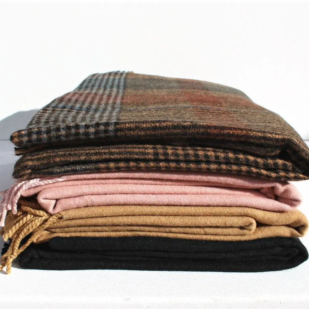 Stack of plaid and solid color blankets on a white background. Throw Scarf Tweed - The Rose Edit