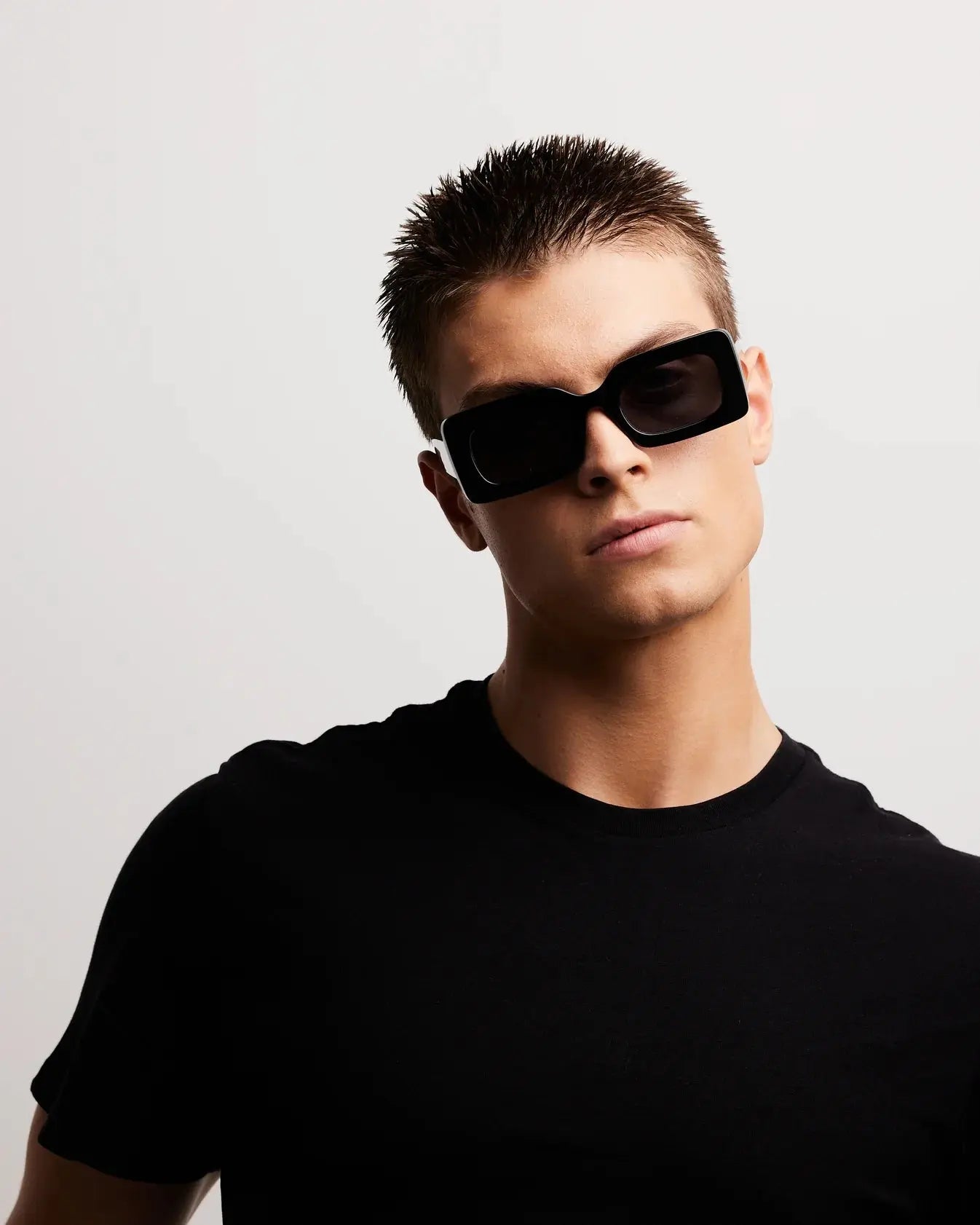 Person wearing black sunglasses and a black shirt against a light gray background