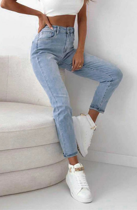 Person wearing light blue jeans and white sneakers sitting on a gray sofa.