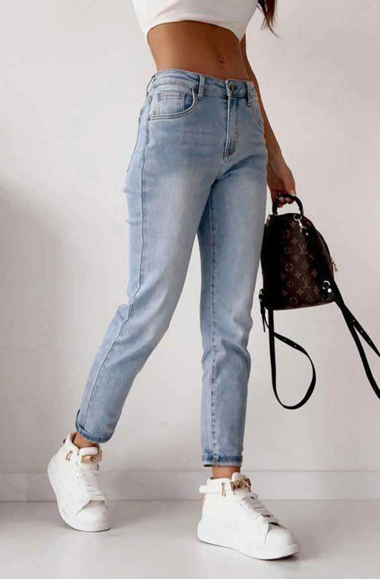 Person wearing light blue jeans and white sneakers with a black handbag on a plain background