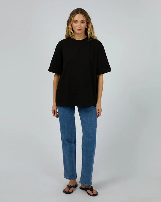 Person wearing a black t-shirt and blue jeans on a plain background. Core Oversized Tee Black - The Rose Edit