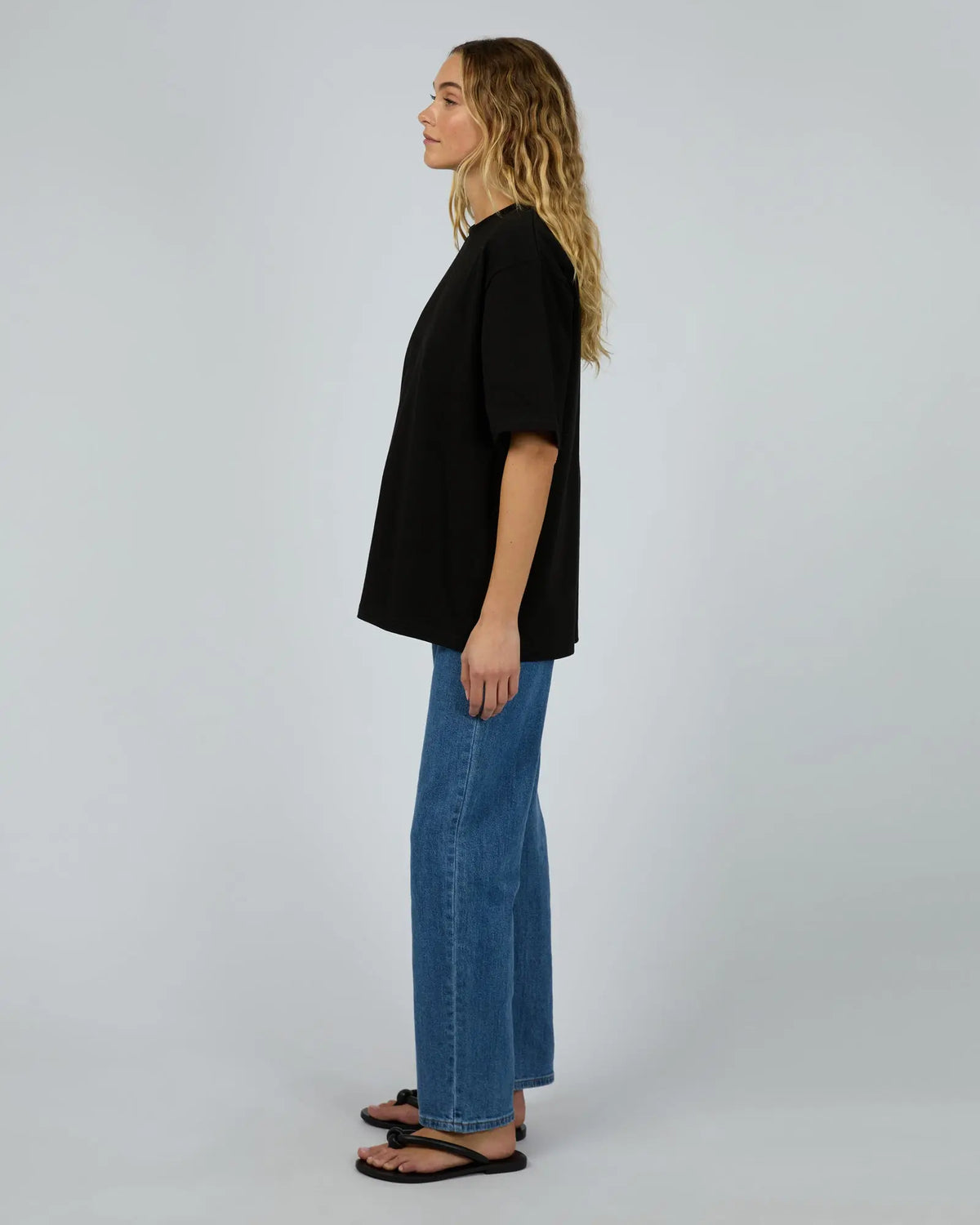 Person wearing a black t-shirt and blue jeans standing against a plain background.Core Oversized Tee Black - The Rose Edit