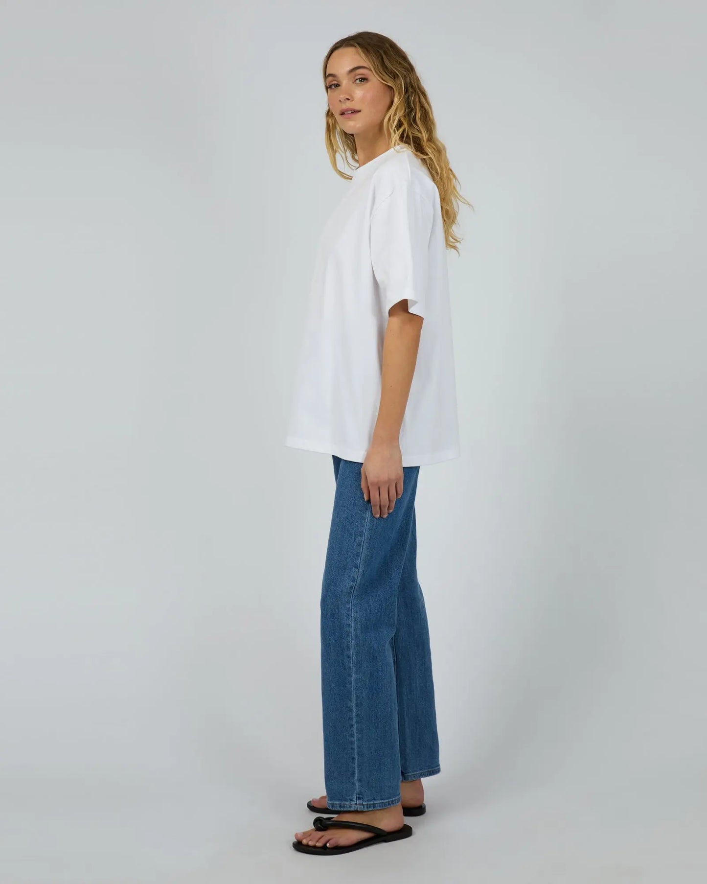 Woman wearing a white shirt and blue jeans on a plain background
