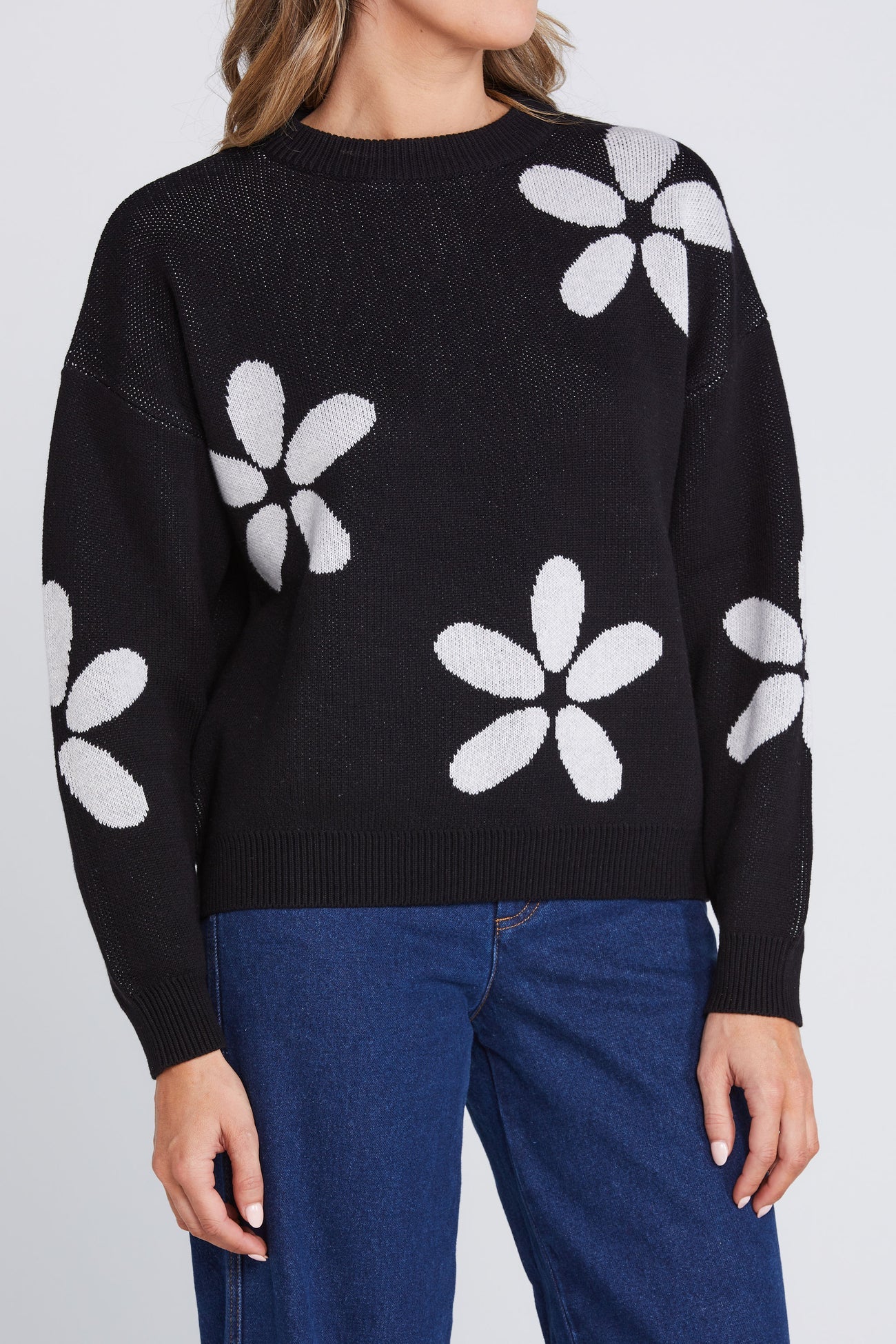 Close-up of the Petal Jumper by Thing Thing — black cotton knit sweater with oversized white petal motifs, styled with blue denim jeans.