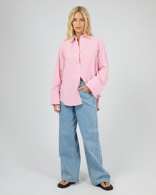 Woman wearing a pink striped shirt and blue jeans on a gray background