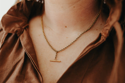 Close-up of a person wearing a gold necklace with a pendant. Large T Bar Necklace KatyB Jewellery